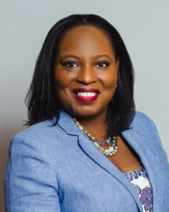 Lavinia Awosanya Headshot Head shot of Lavinia Awosanya, a Black woman in a light blue blazer with a white and blue shirt and earth tone necklaces. She is looking straight on the camera with a smile on her face.