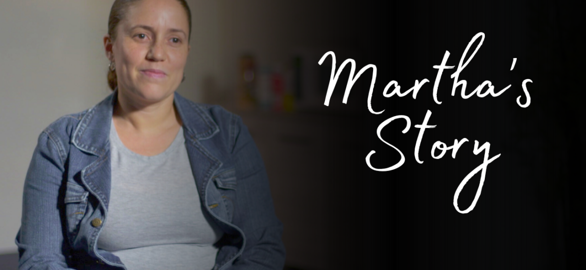 Picture of a Latina woman in a blue jean jacket and gray shirt. She is making a neutral face. On the right side of the screen, there is white text on a black background that reads "Martha's Story."