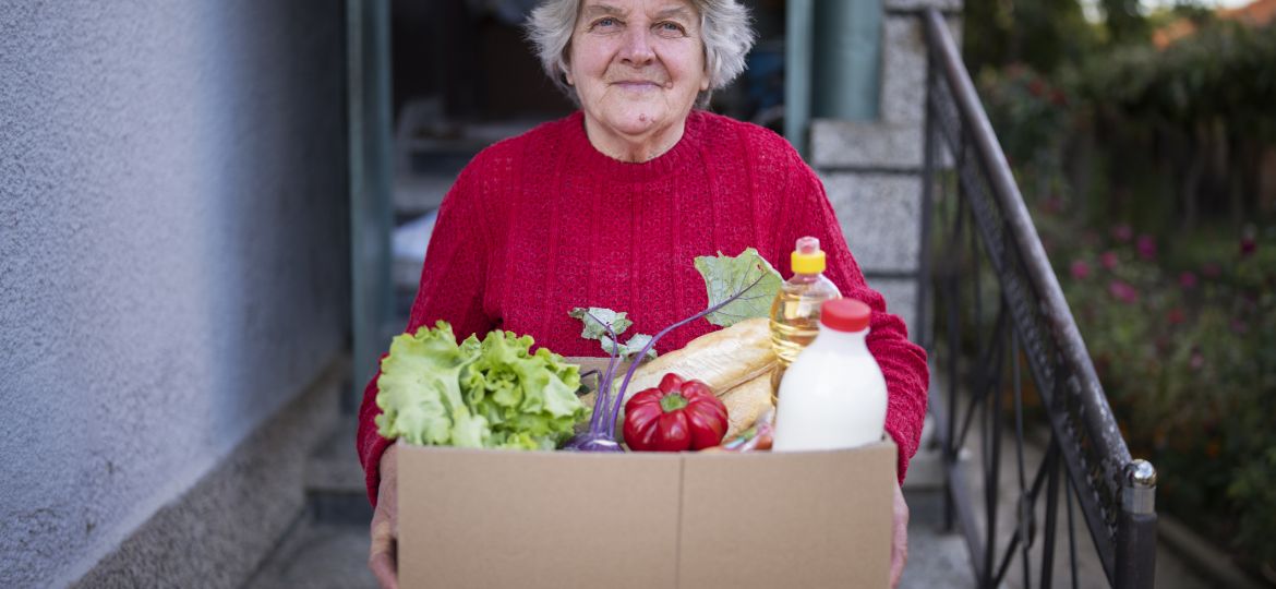 Portrait of happy senior woman with received crate with food during pandemic.